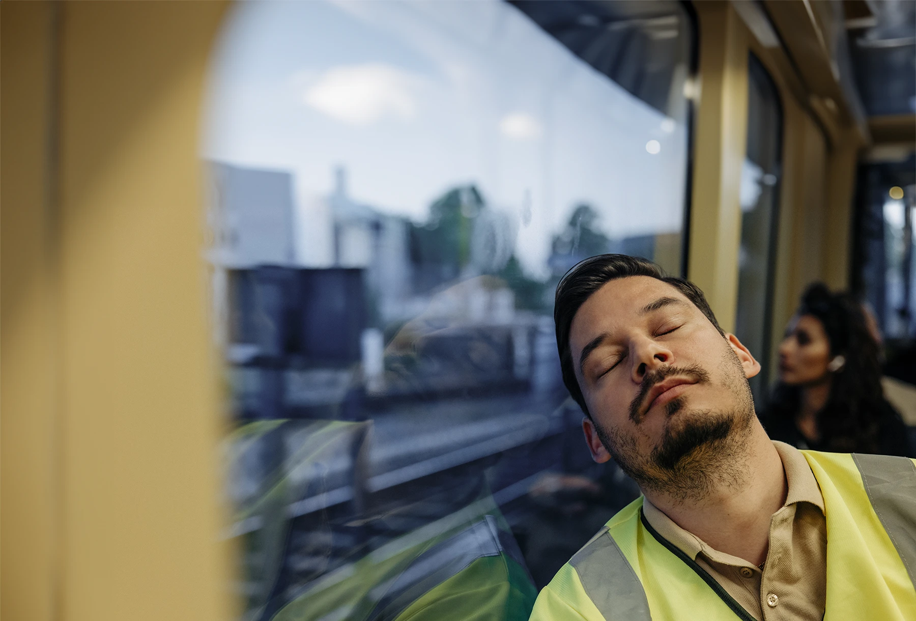 Young Hispanic man with reflective jacket sleeps on a tram.