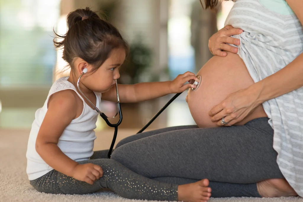 Cute toddler listens to mom's pregnant belly using a stethoscope.