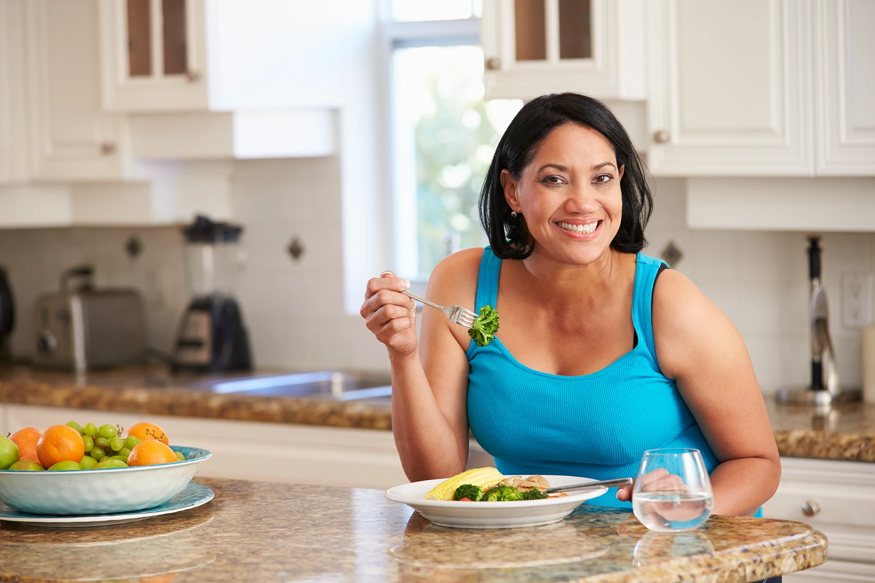 Smiling Hispanic woman eats a meal of plant based foods.