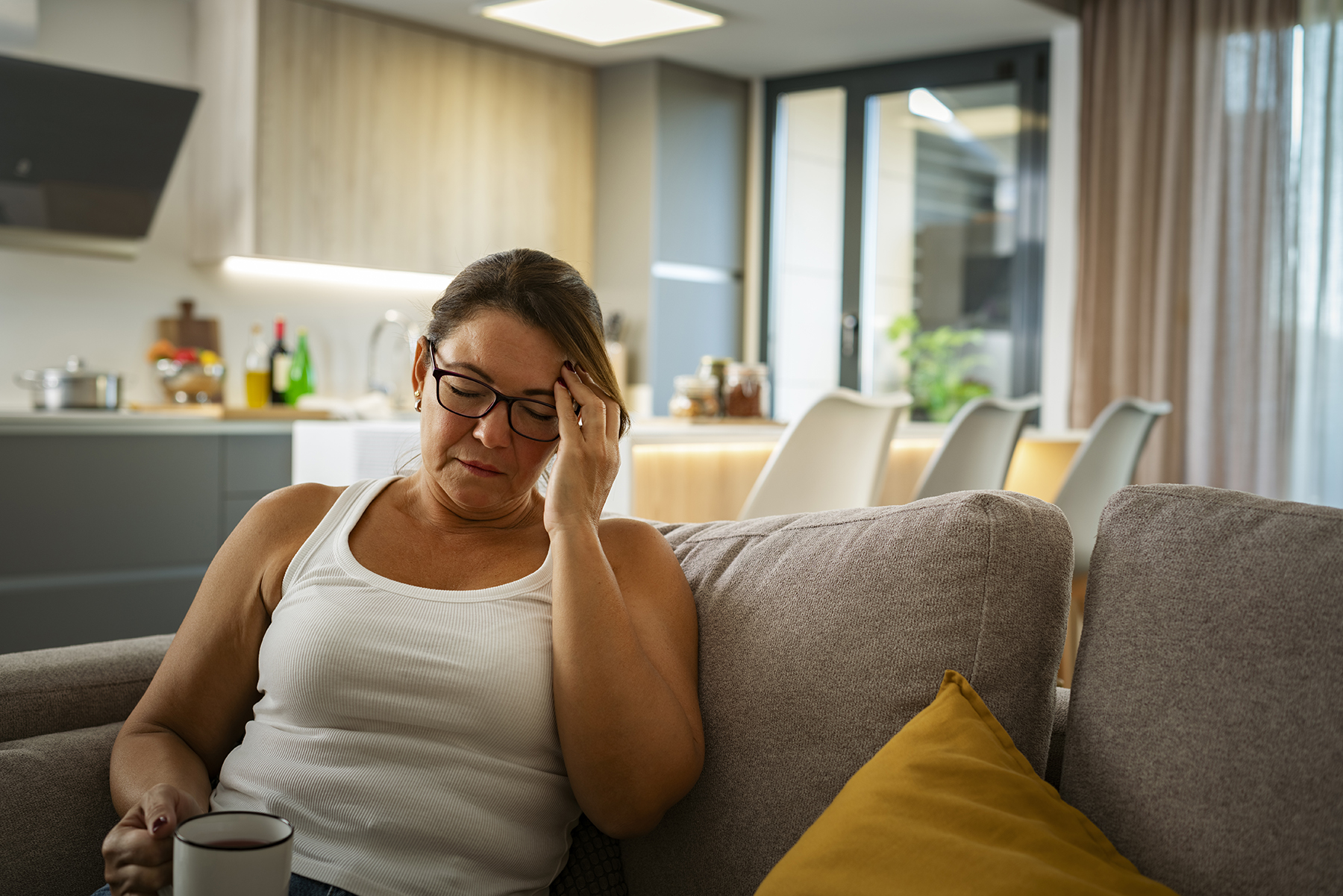 Hispanic woman sits on couch, dealing with chronic fatigue.