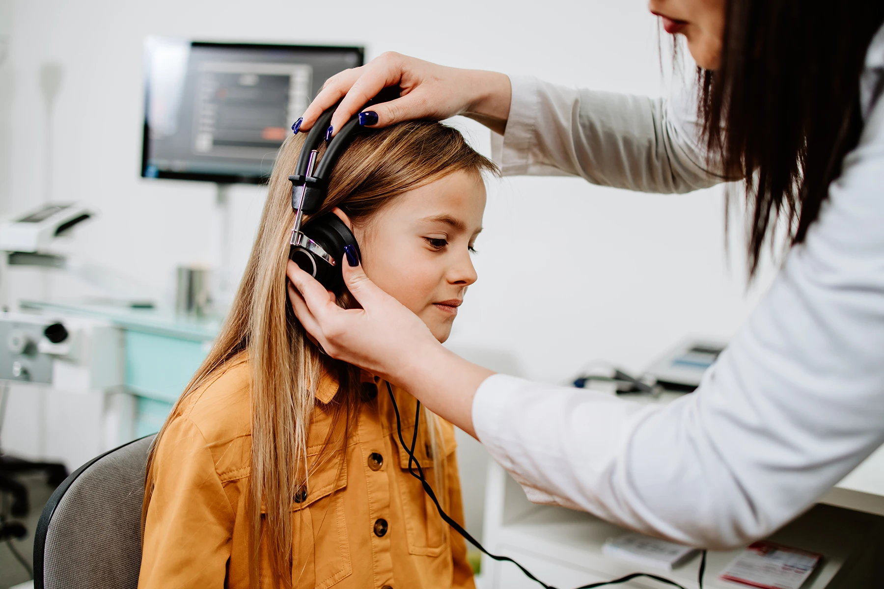 Young teenage girl sits for a hearing test at an audiologist's office.