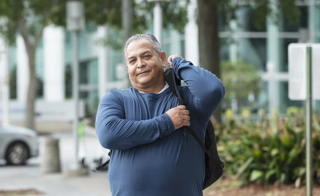 Heavyset mature Hispanic man carries backpack in city. Extra weight gain can contribute to a number of health conditions, including diabetes and OSA.