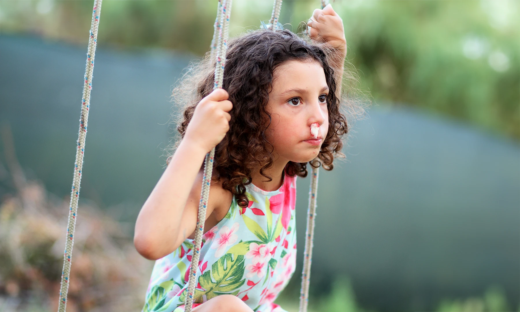 Little girl sits on swing with a tissue in her nose to slow a nosebleed.