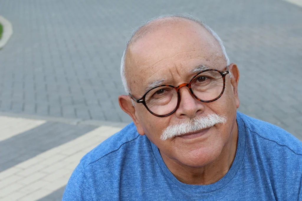 Senior Hispanic man in glasses peers at photographer