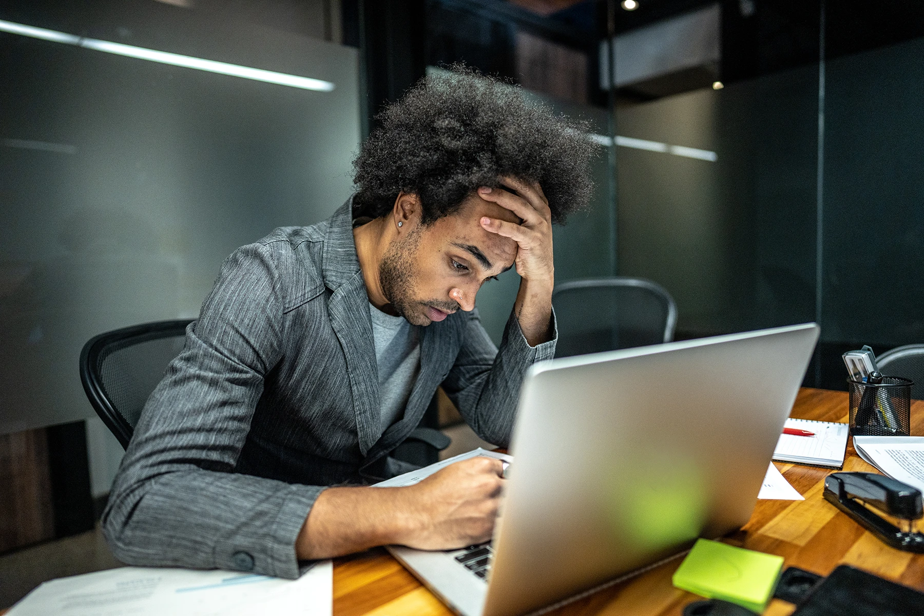 Stressed Hispanic man sits at desk with hand on head, depicting job stress