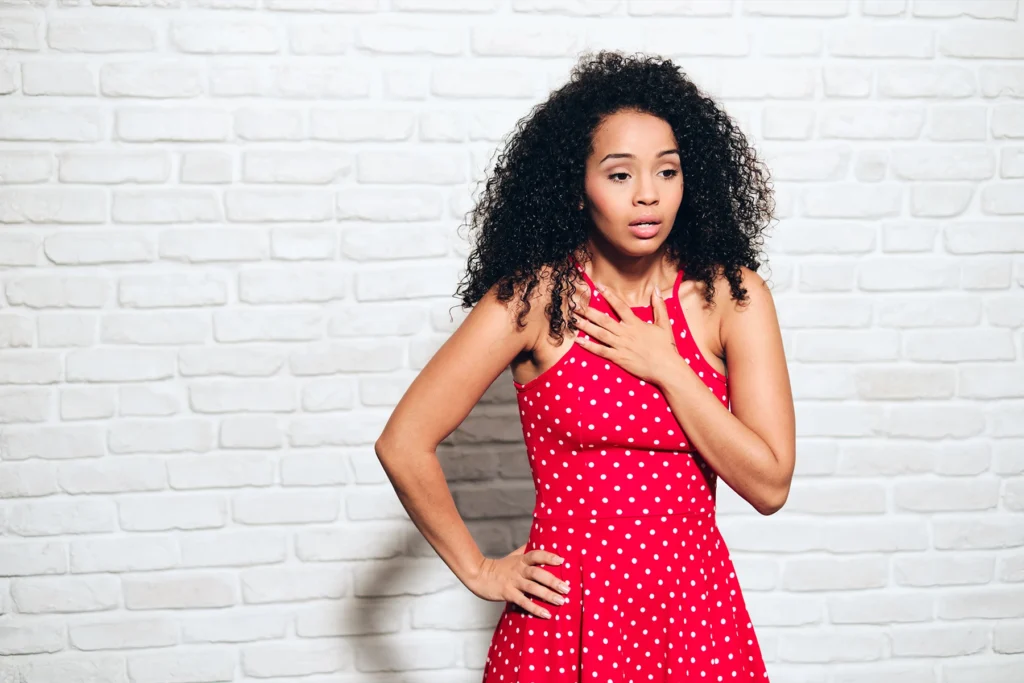 Woman in red dress holds her hand to her chest, feeling short of breath.