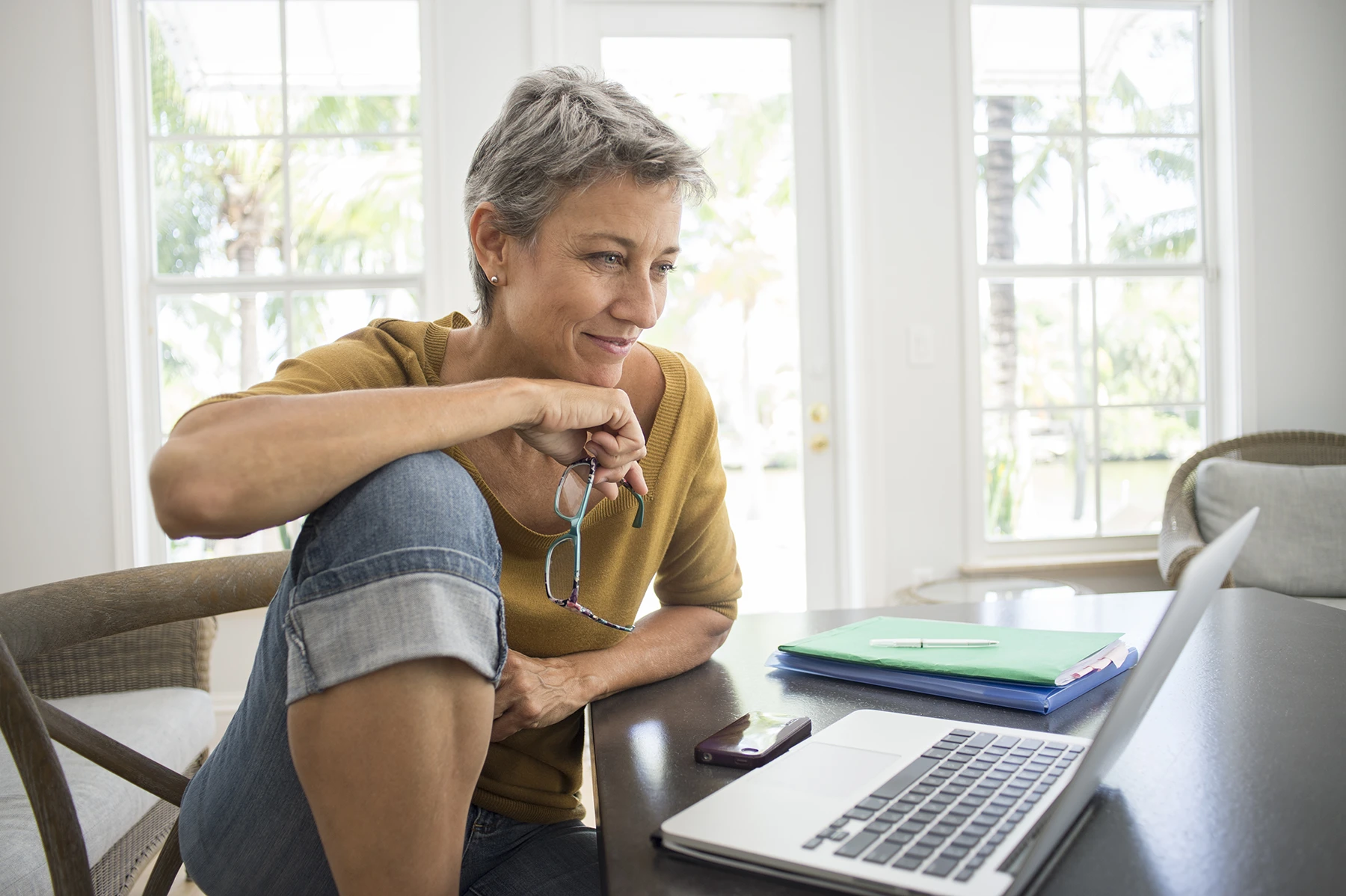 Woman with short gray hair smiles as she researches aging and skin on her laptop