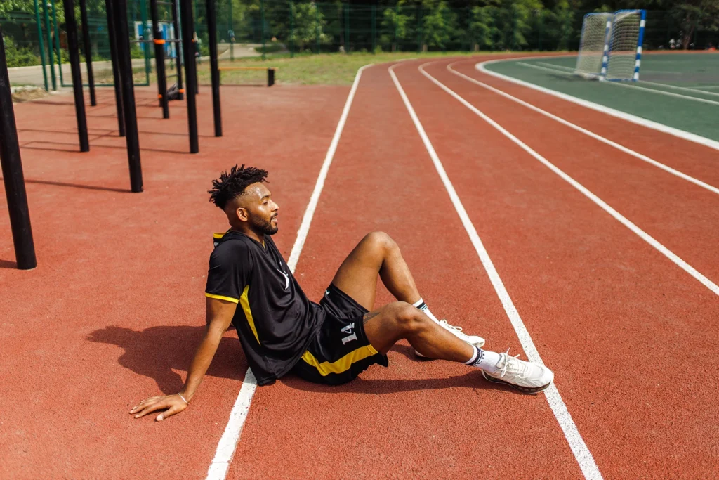 Young, fit Black man sits on the edge of a running track, resting.