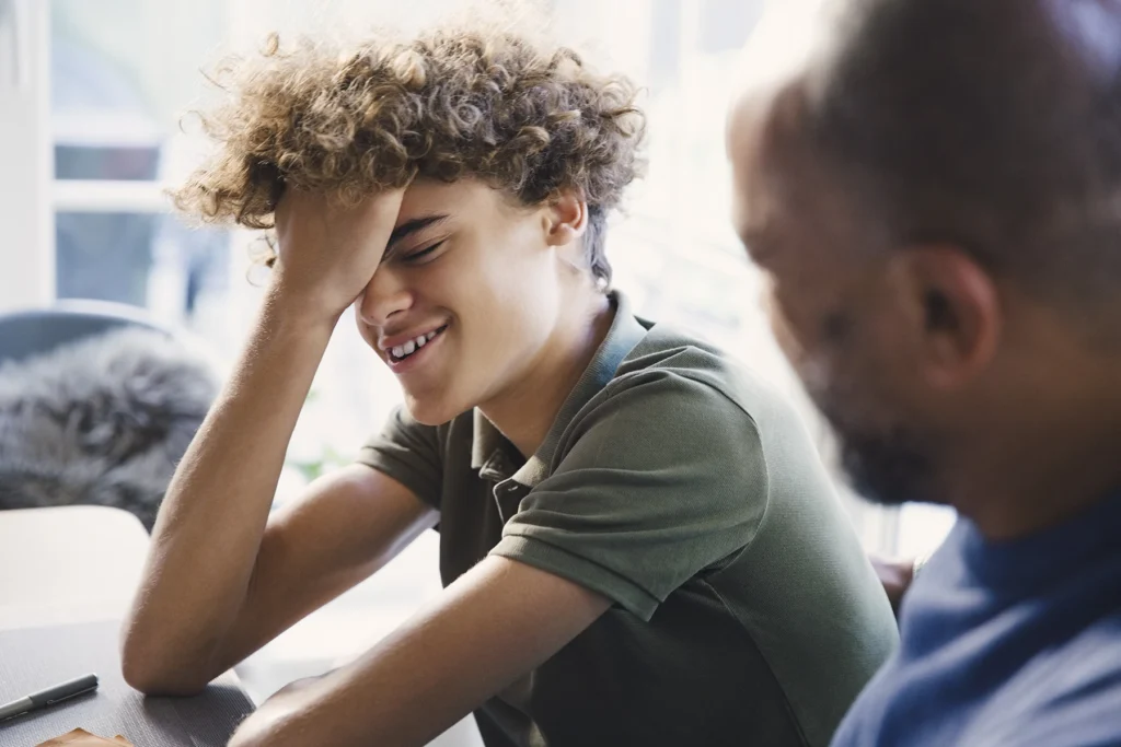 Teen boy embarrassed by sex talk with dad. Holds hand to face at the awkwardness.