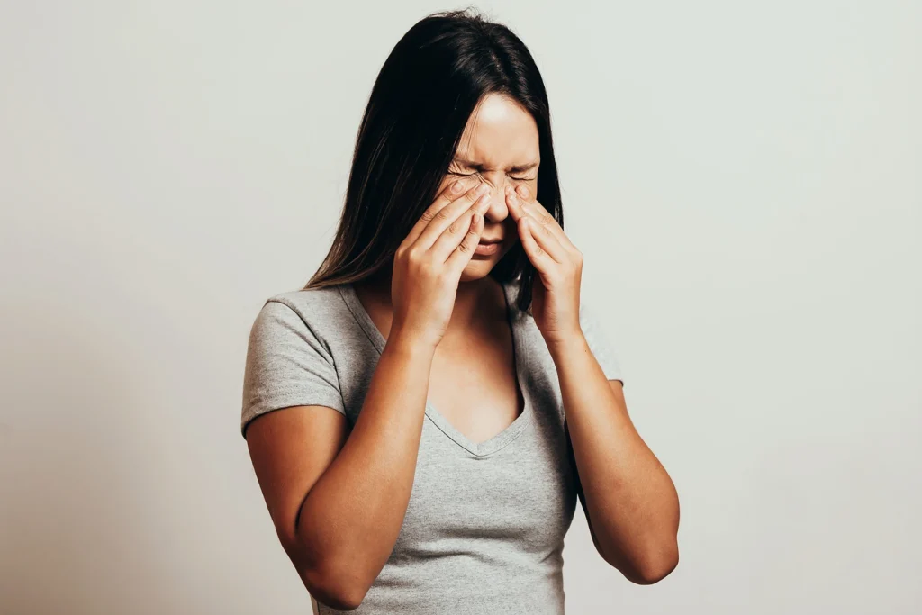 Woman squeezes her upper nasal passages due to rhinitis pain. Illustrative stock image.