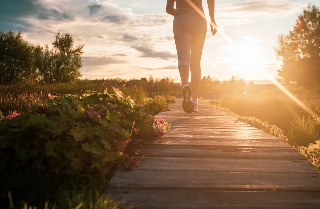 Woman walking for exercise down a beach walkway as the sun rises.