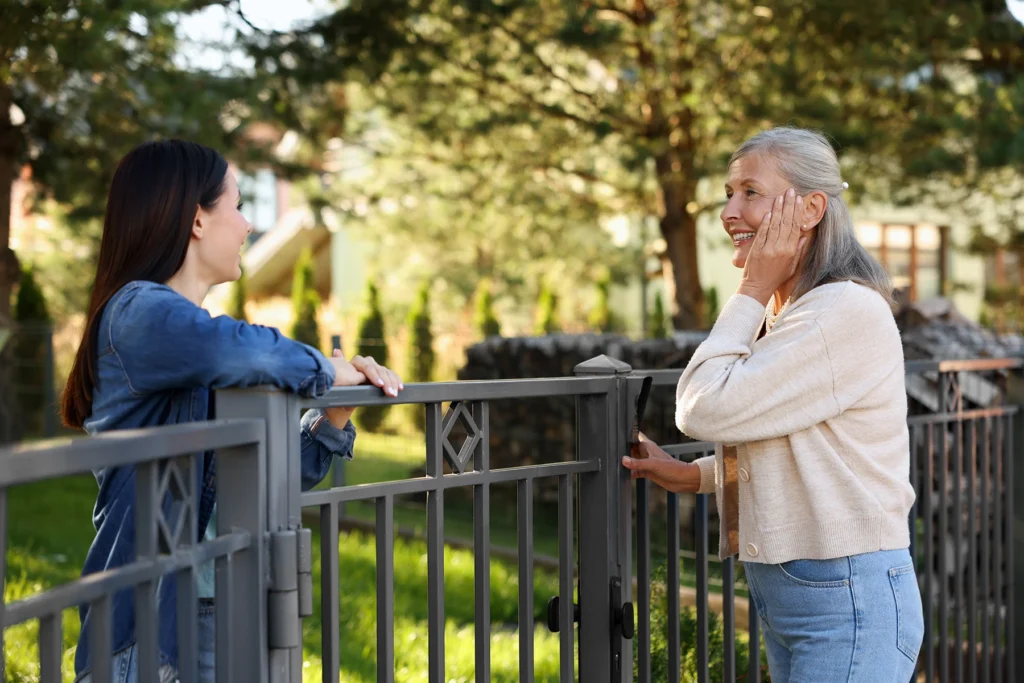 two women neighbors have a friendly chat over a fence.