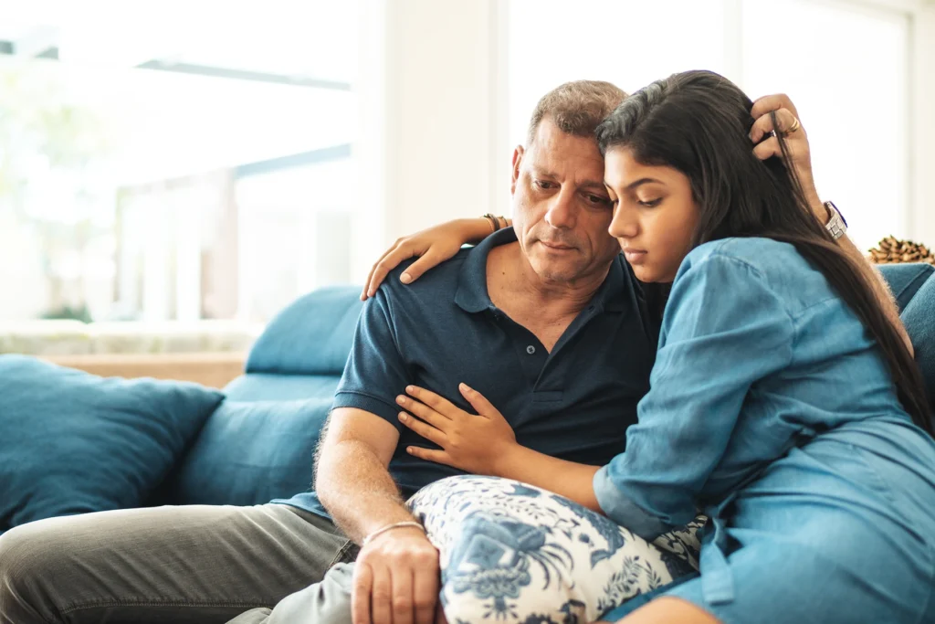 Dad and daughter, sitting together on couch, support each other through grief.