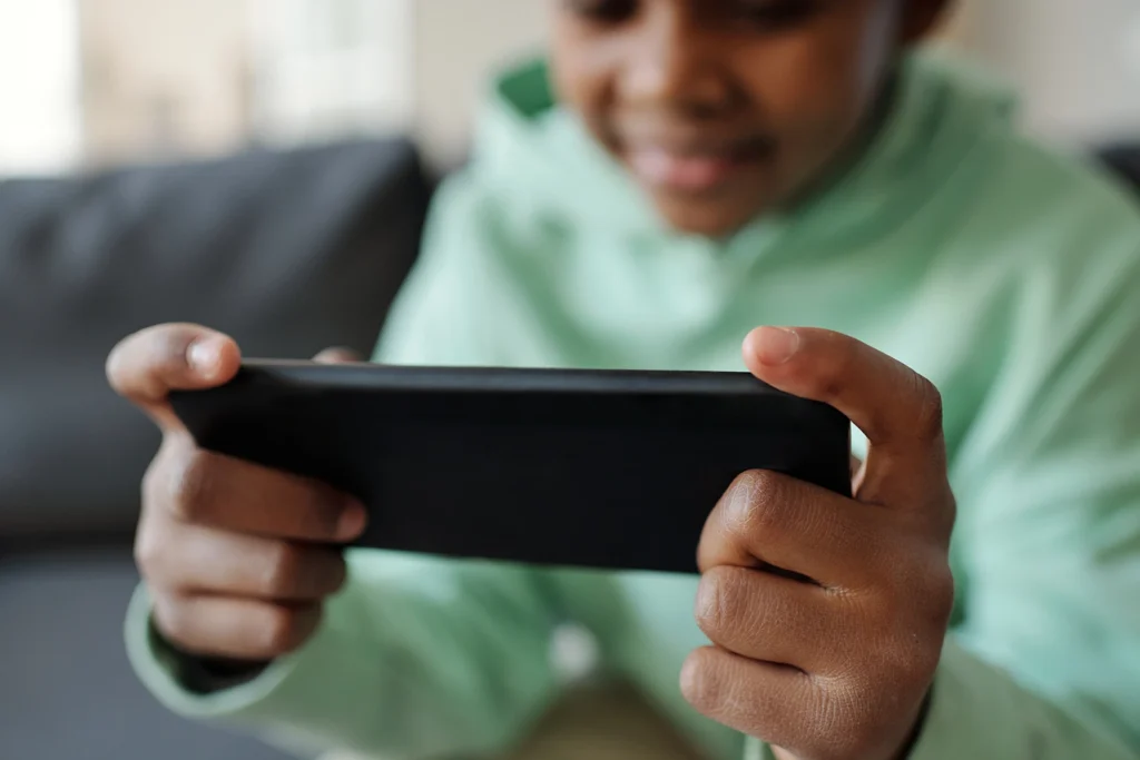 Close up on phone that is being held by a young Black child playing games. Illustrating screentime.