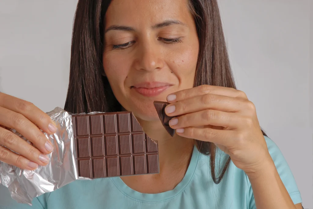 Middle-aged woman smiles breaking off a piece of dark chocolate.