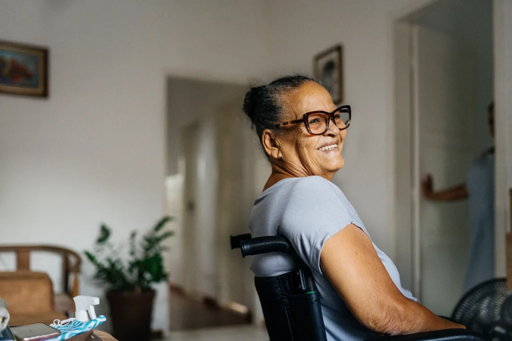 Elderly Hispanic woman smiles while sitting in a wheelchair.