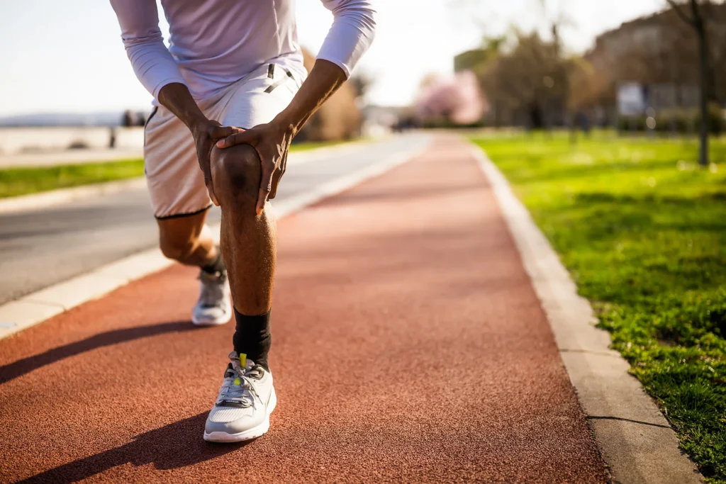 Black man stops running on track and holds his aching knee.