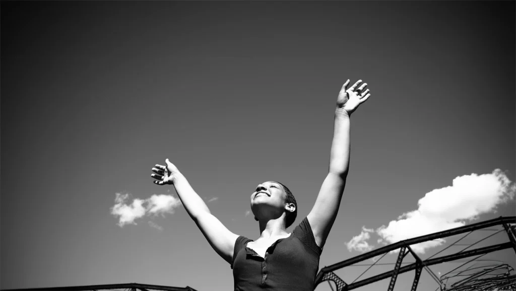 Black and white shot of woman holding hands to the sky in praise. Healing power of faith