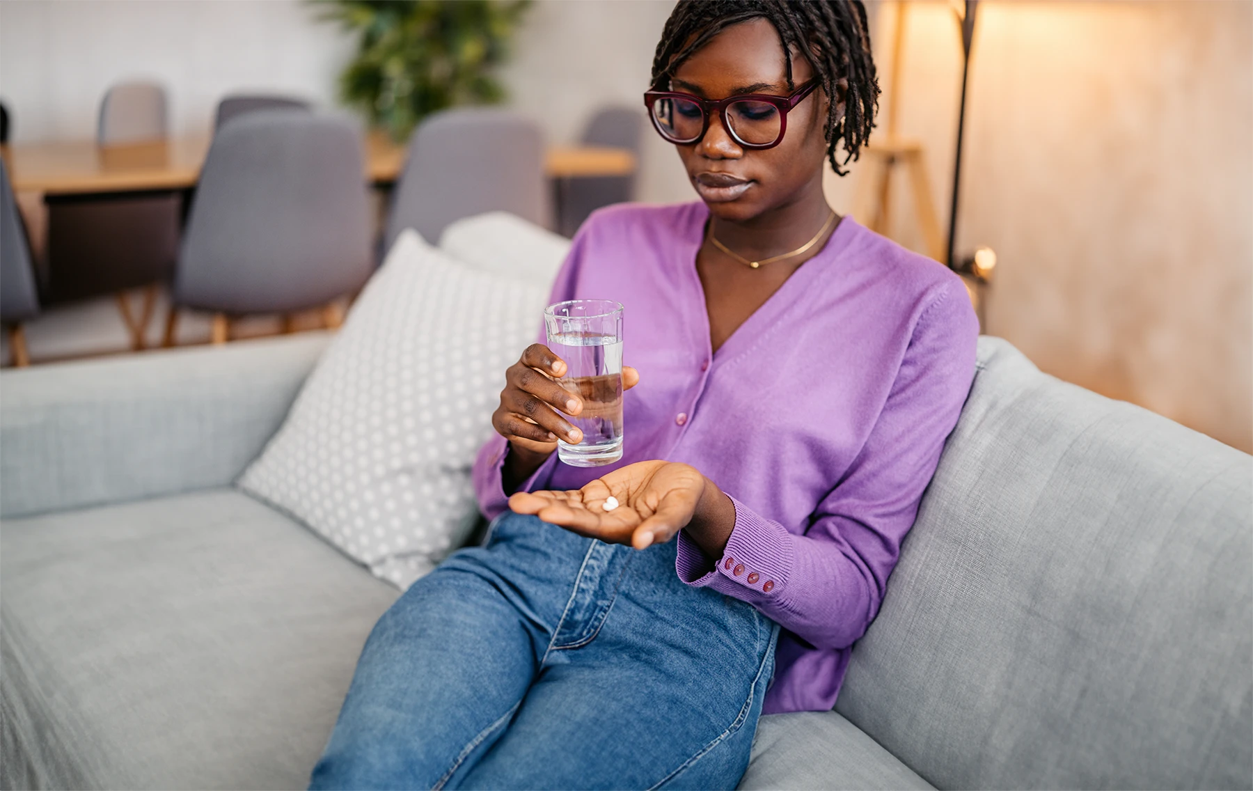 Young Black woman sits on couch and takes antibiotics with a glass of water.