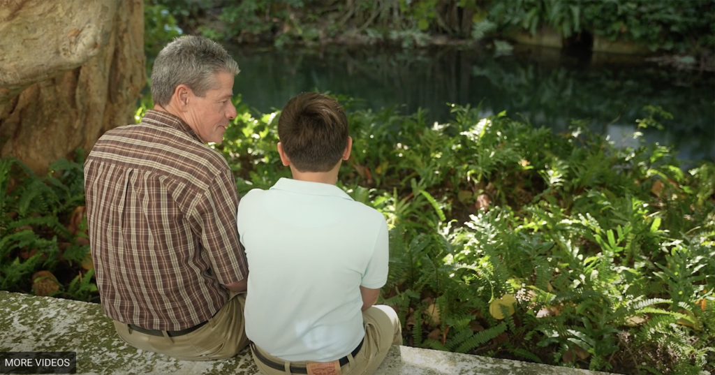 JJ Herrán and young boy sit outside and talk.