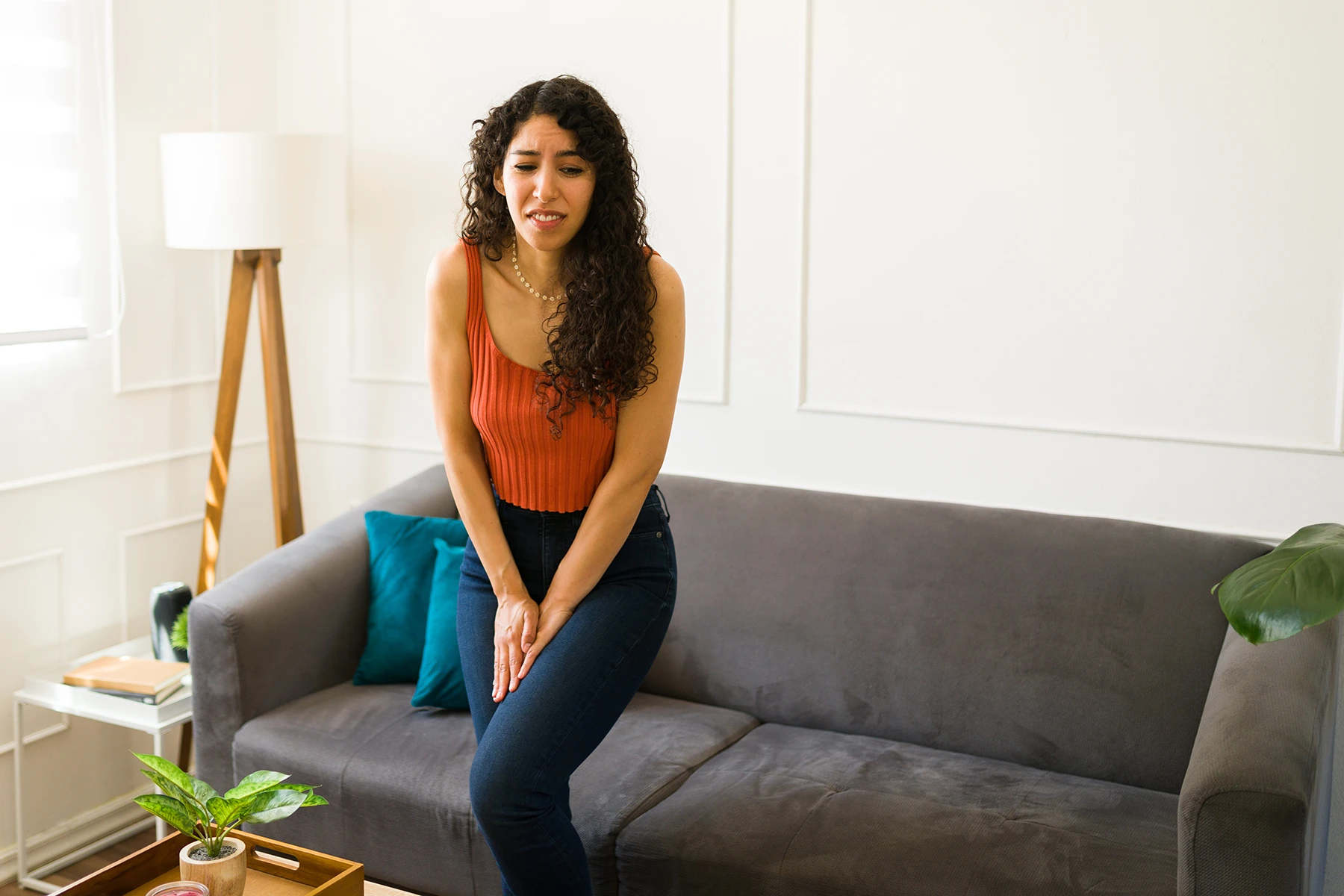 Hispanic woman stands with legs crossed, araid to leak pee, due to urinary incontinence.