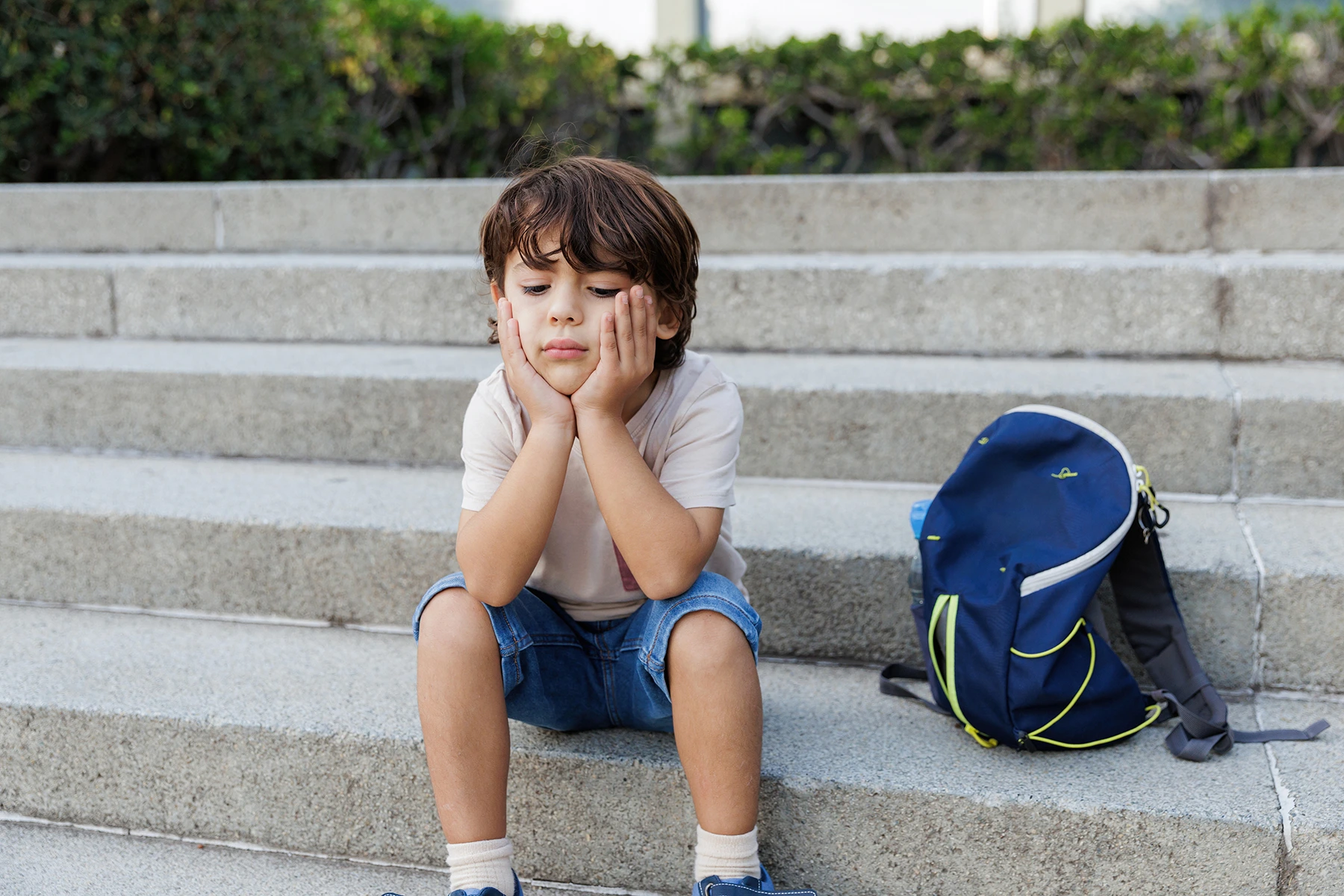 Sad little boy sits on stairs.