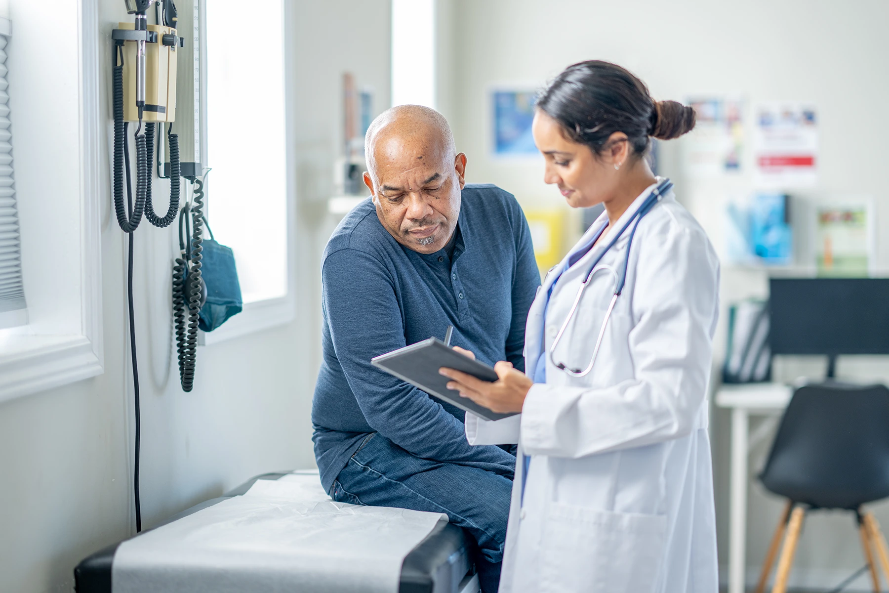 Doctor sits on patient bed while talking to doctor about his test results.
