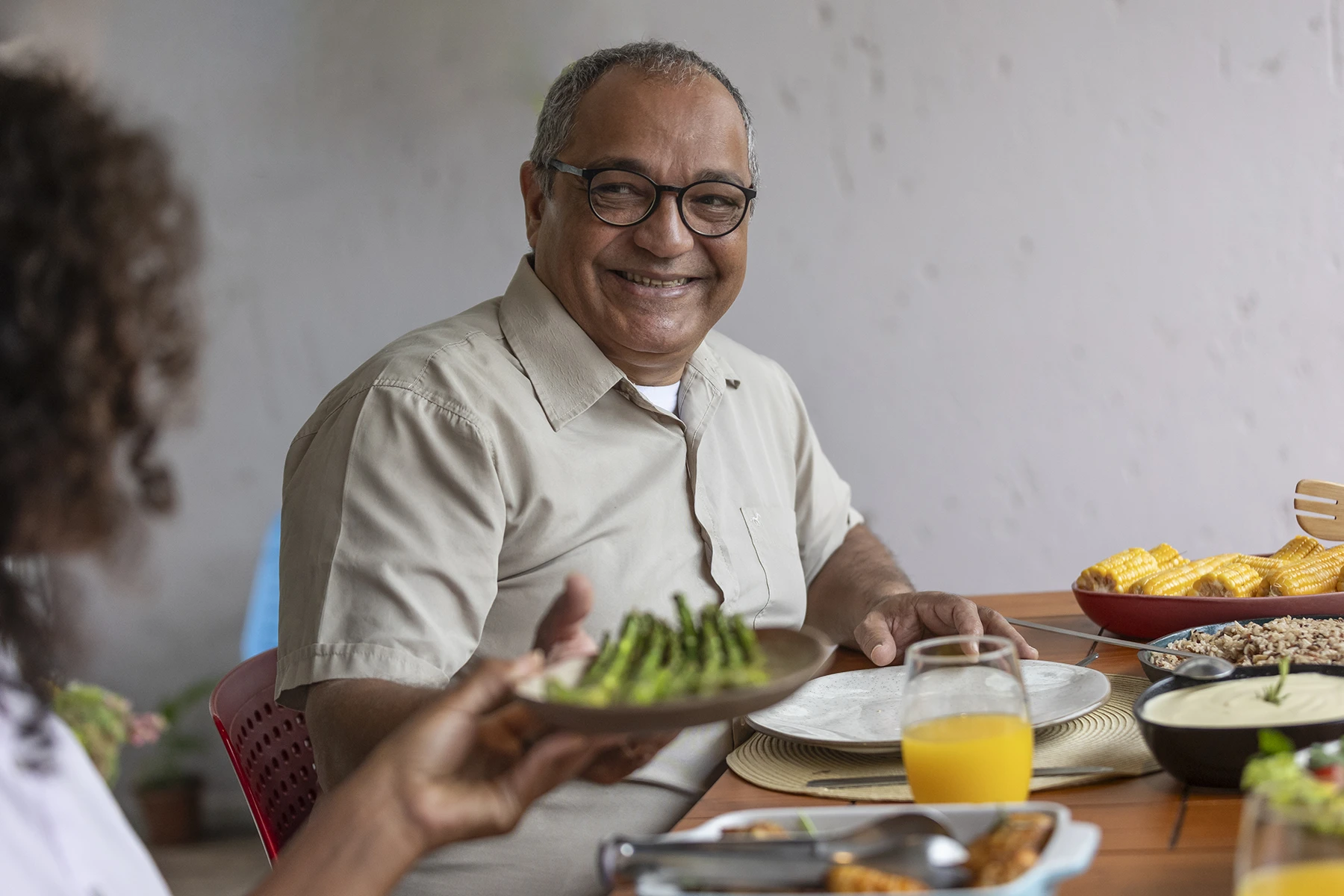 Happy Hispanic father accepts a plate of asparagus being passed at the dinner table.