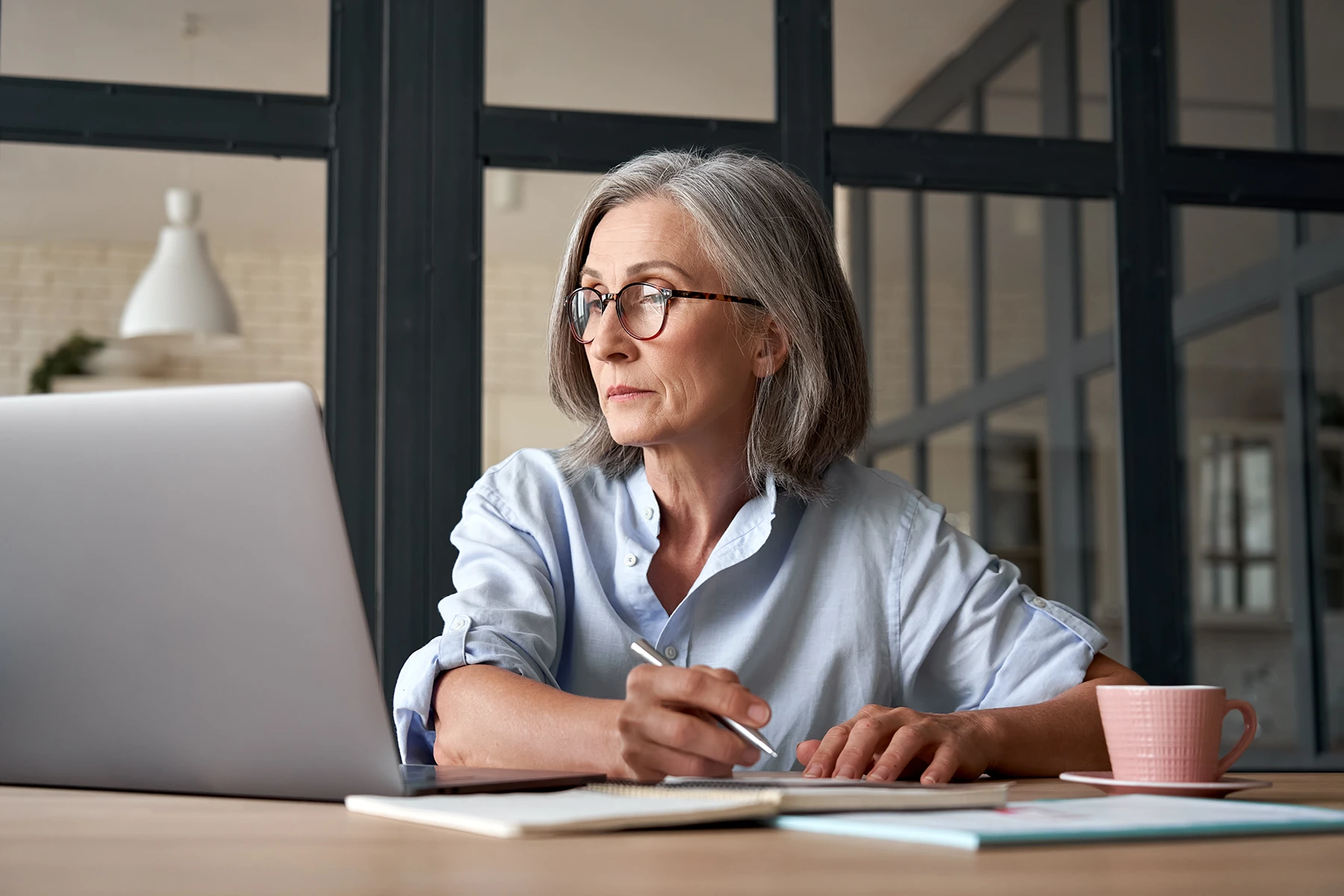 Serious senior woman reads information on her laptop.