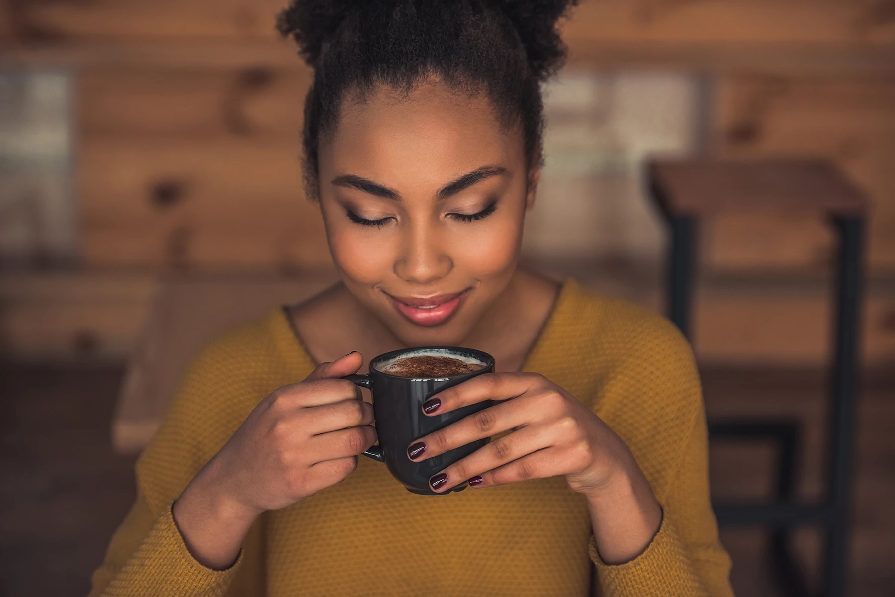 Young black woman smiles, appreciating the small of her coffee in a cute cafe.