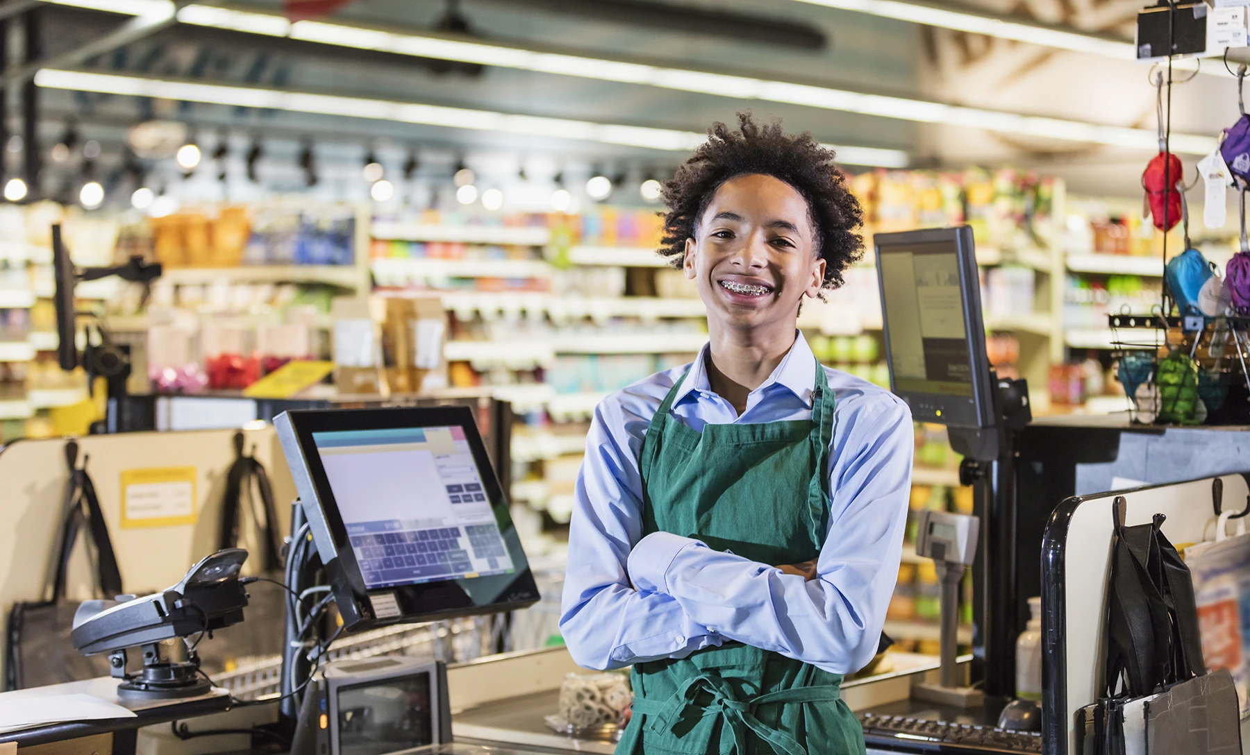 Young teen boy smiles widely working as a cashier at a grocery store.