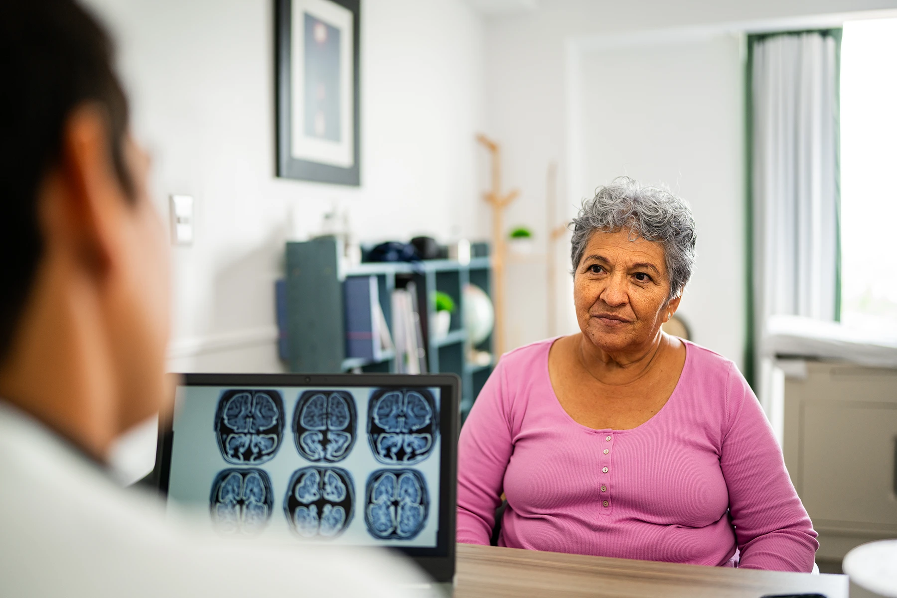Older Hispanic woman consults with a doctor who is reviewing brain scans.