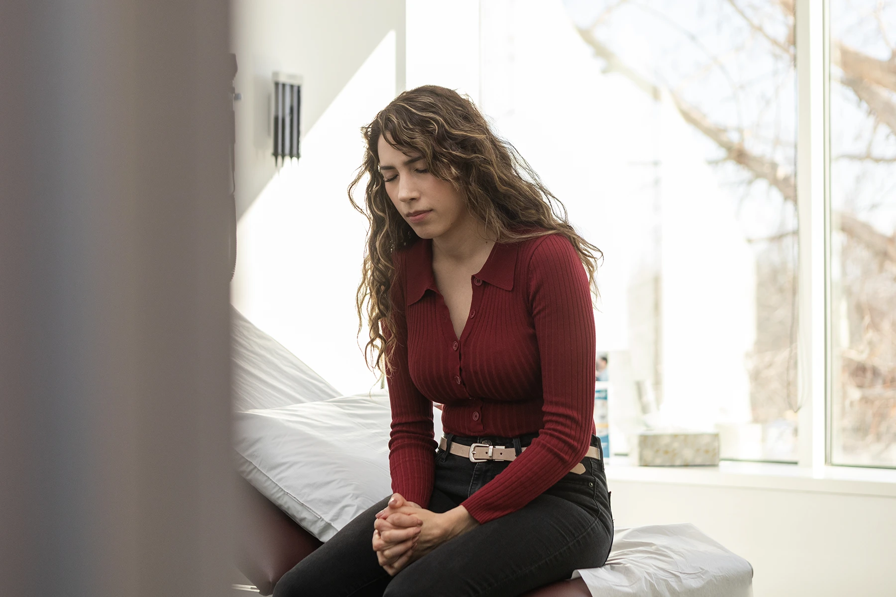 Pretty Hispanic woman sits on doctor's exam table, praying, waiting on results from diagnostic scan.