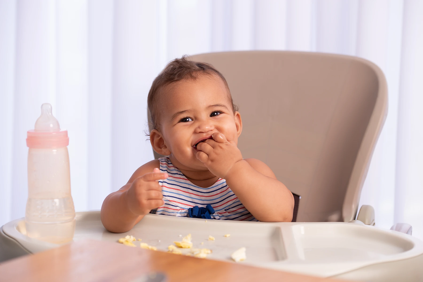 Adorable baby sits in high chair feeding himself.