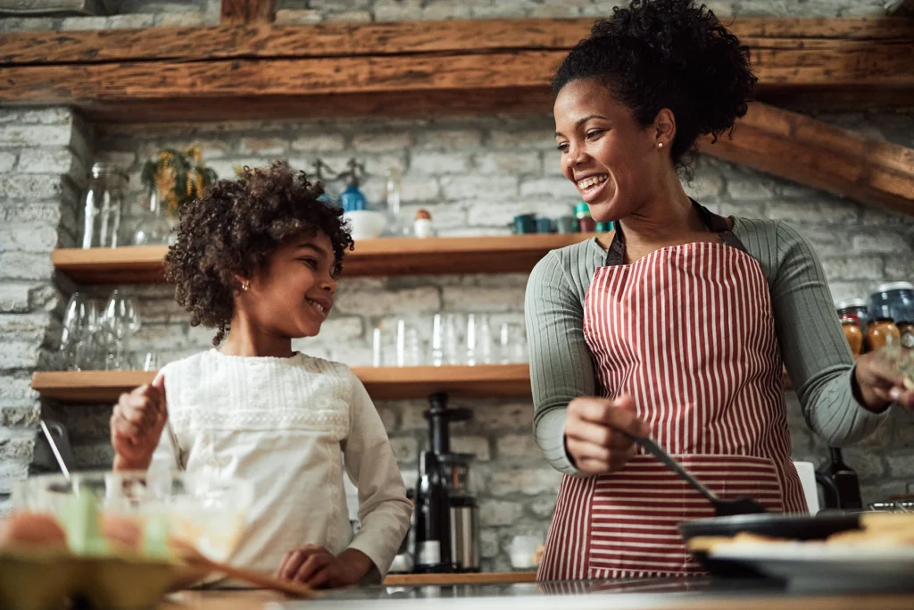 Happy black mother and daughter preparing pancakes in the kitchen. - stock photo