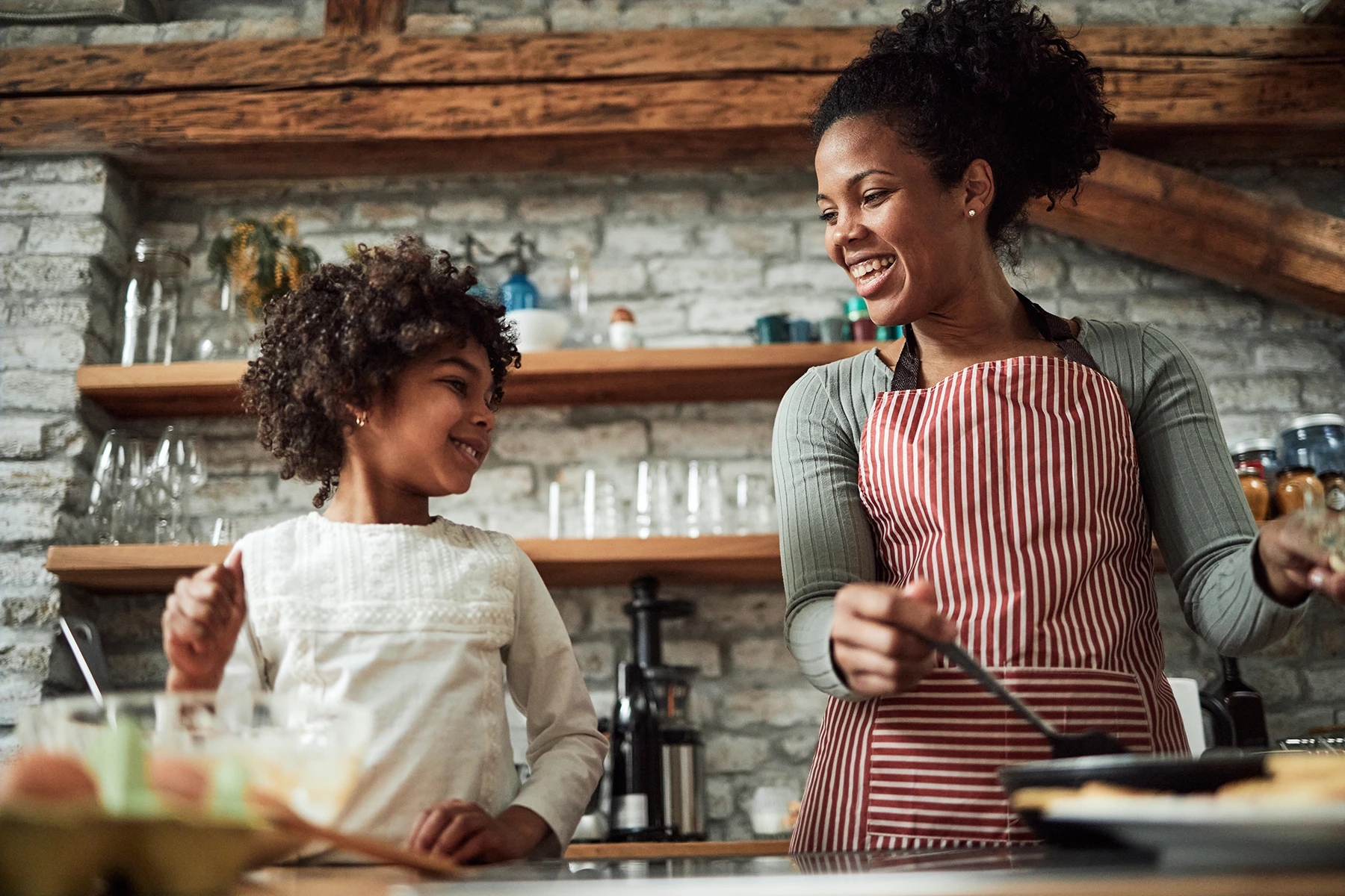 Happy black mother and daughter preparing pancakes in the kitchen. - stock photo