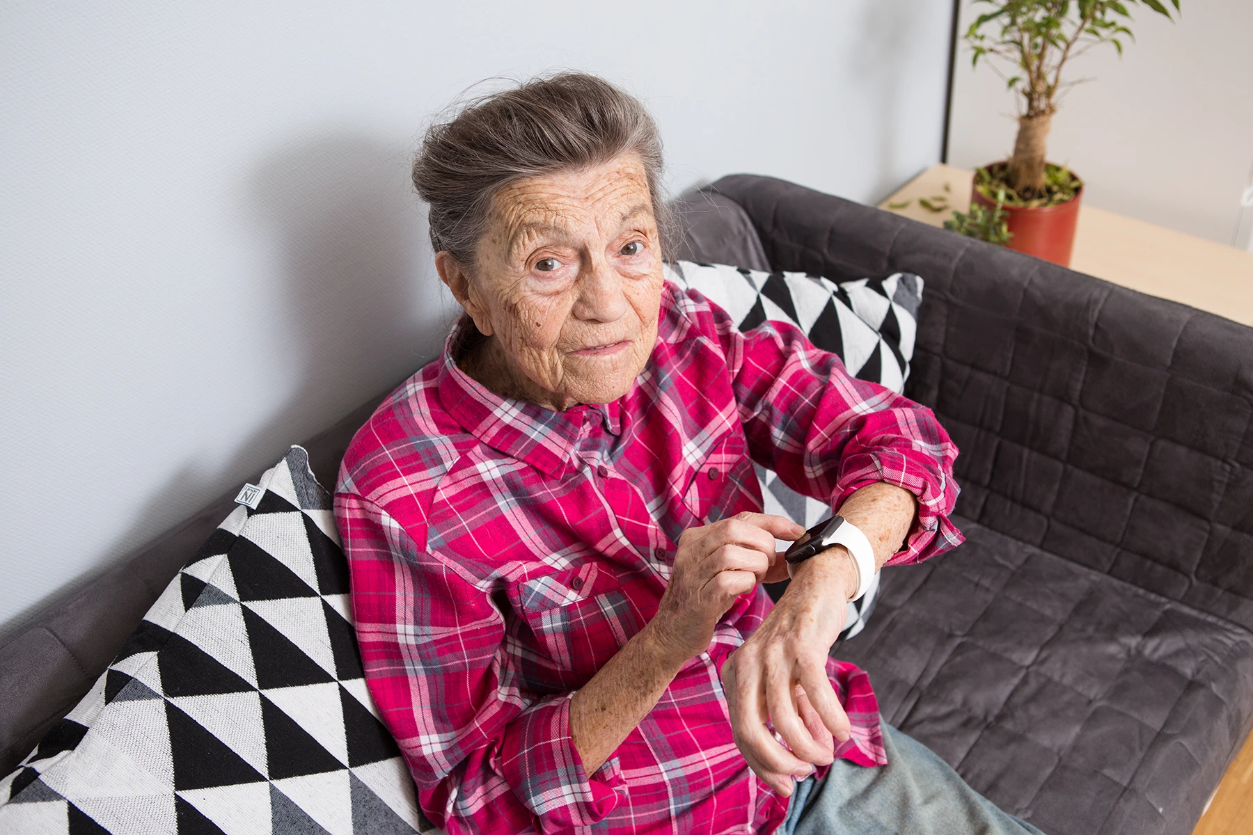 Elderly woman sits on couch and checks her smartwatch.