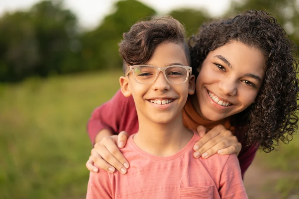 Smiling Hispanic kids pose for the camera while playing outside. The young boy is wearing glasses.