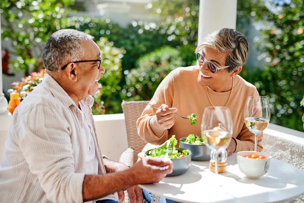 Older couple sits outside, happily eating a healthy lunch.