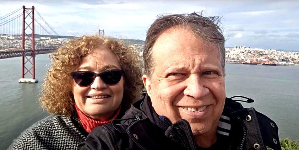 Two people take a selfie with a scenic city view in the background.