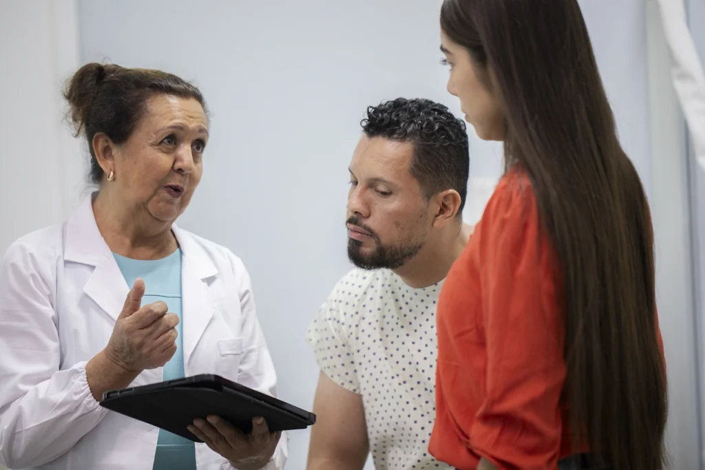Hispanic female doctor talks to male patient and family about possibly entering a cancer clinical trial. Stock image depiction.