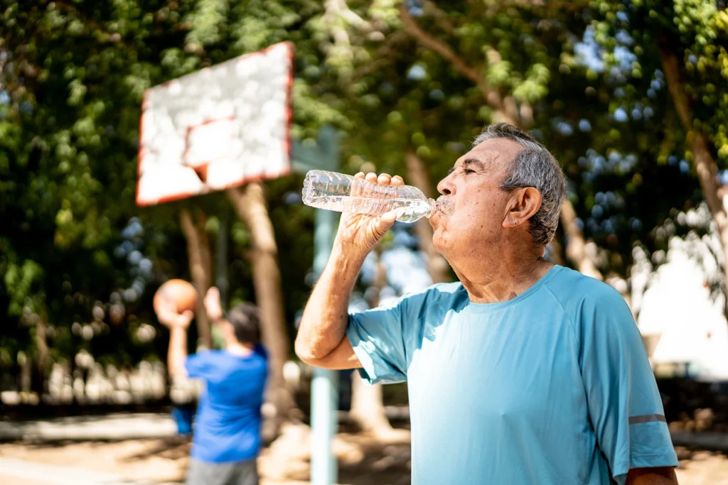 Elderly Hispanic man drinks water to cool down.