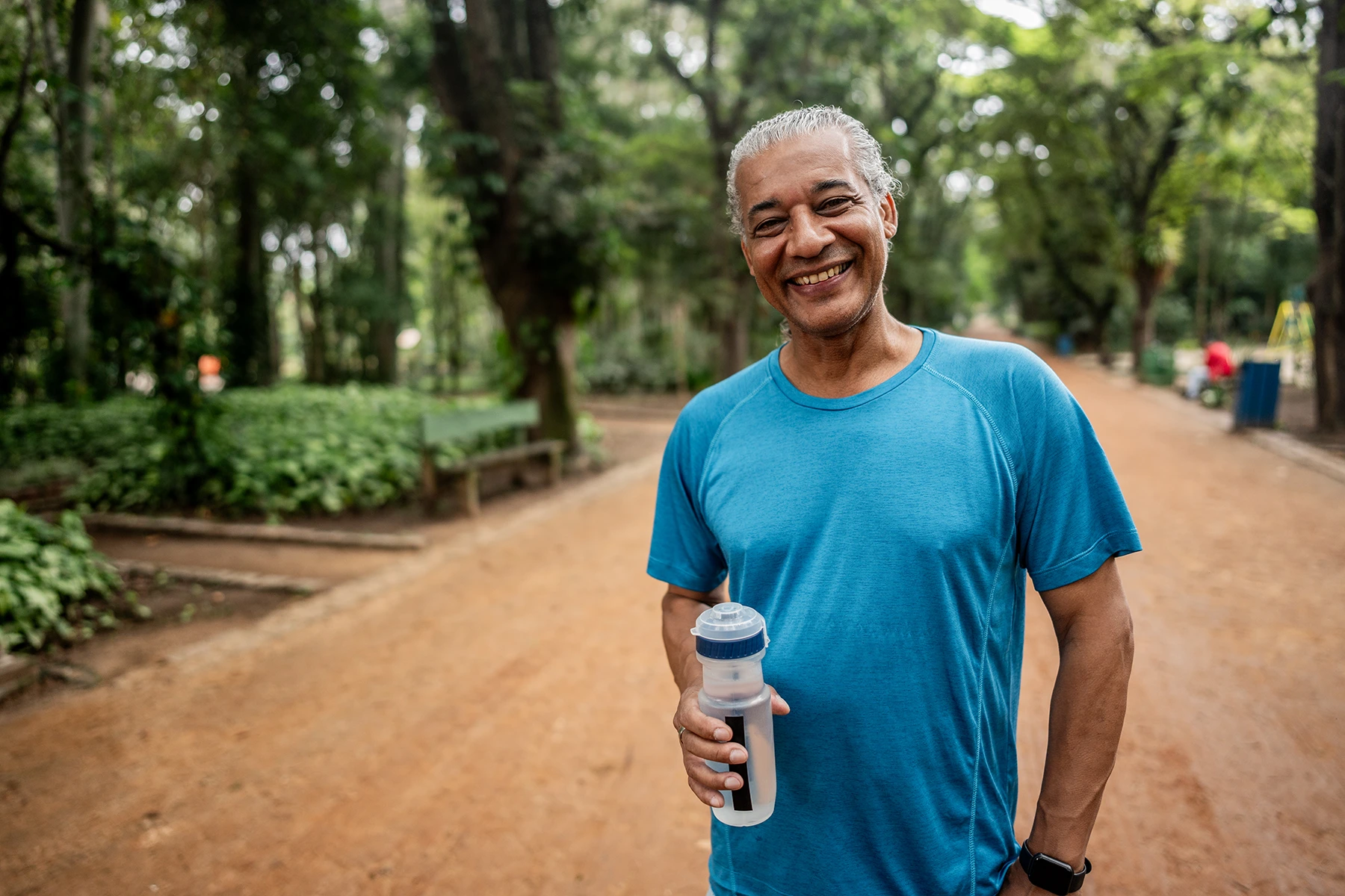 Senior healthy man smiles as he walks outside with a bottle of water.
