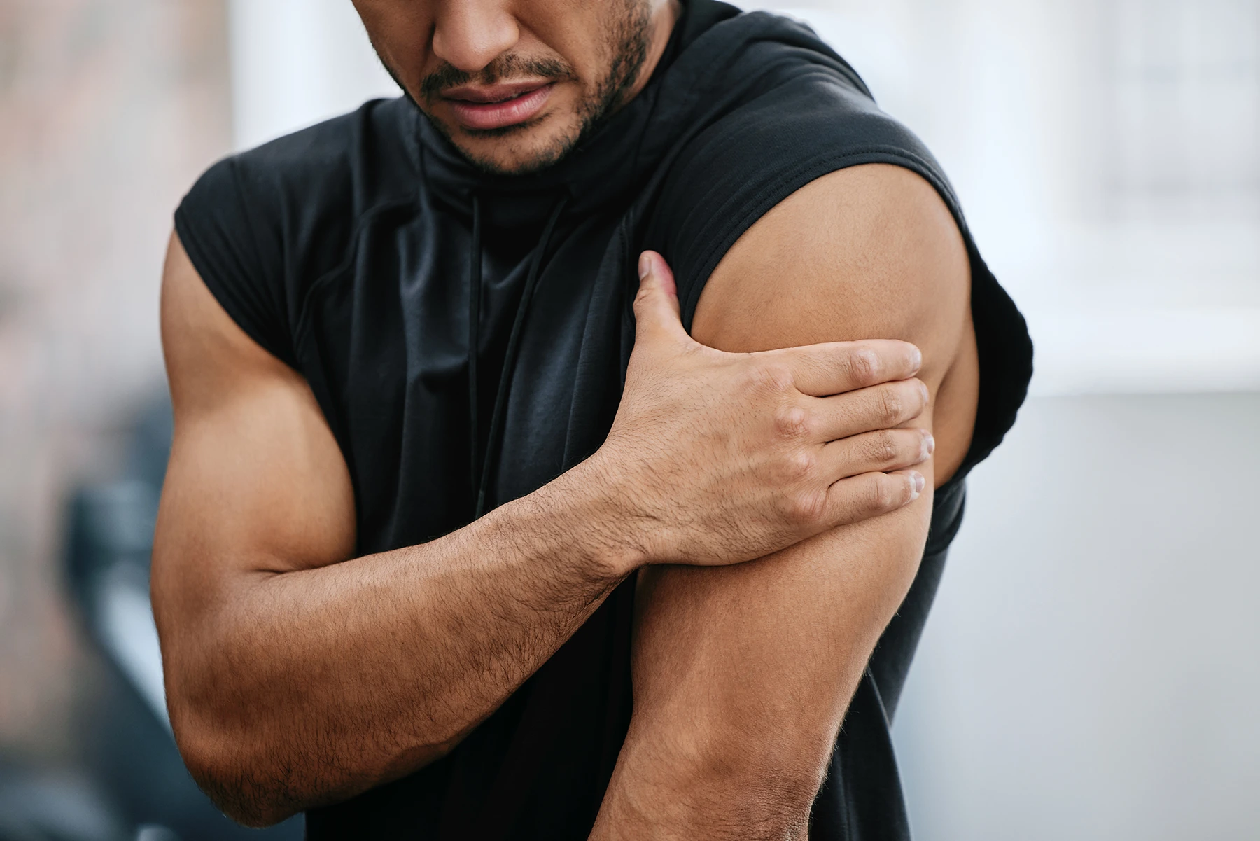 Athletic man has shoulder pain, holds his left shoulder in right hand.