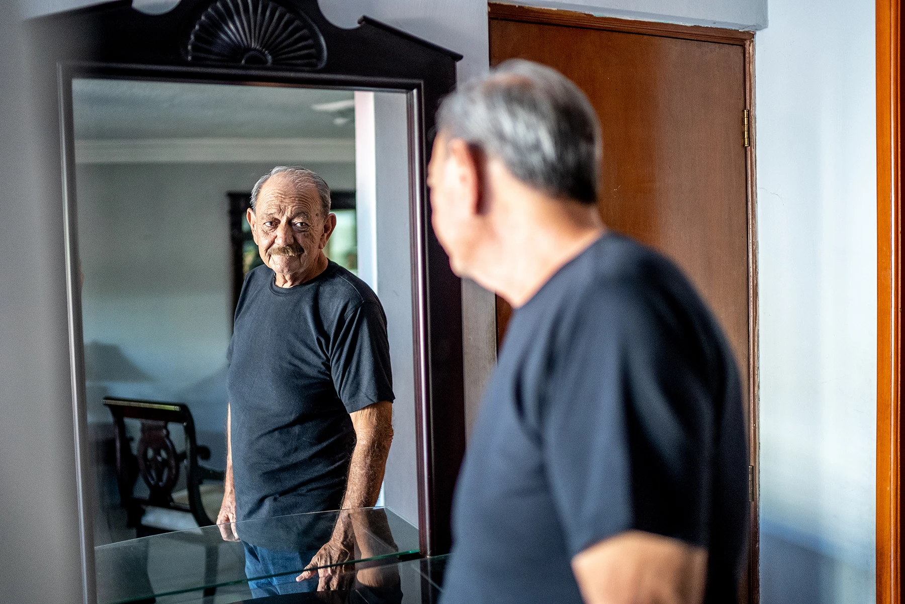 Healthy Hispanic senior man looks at his reflection in the mirror.