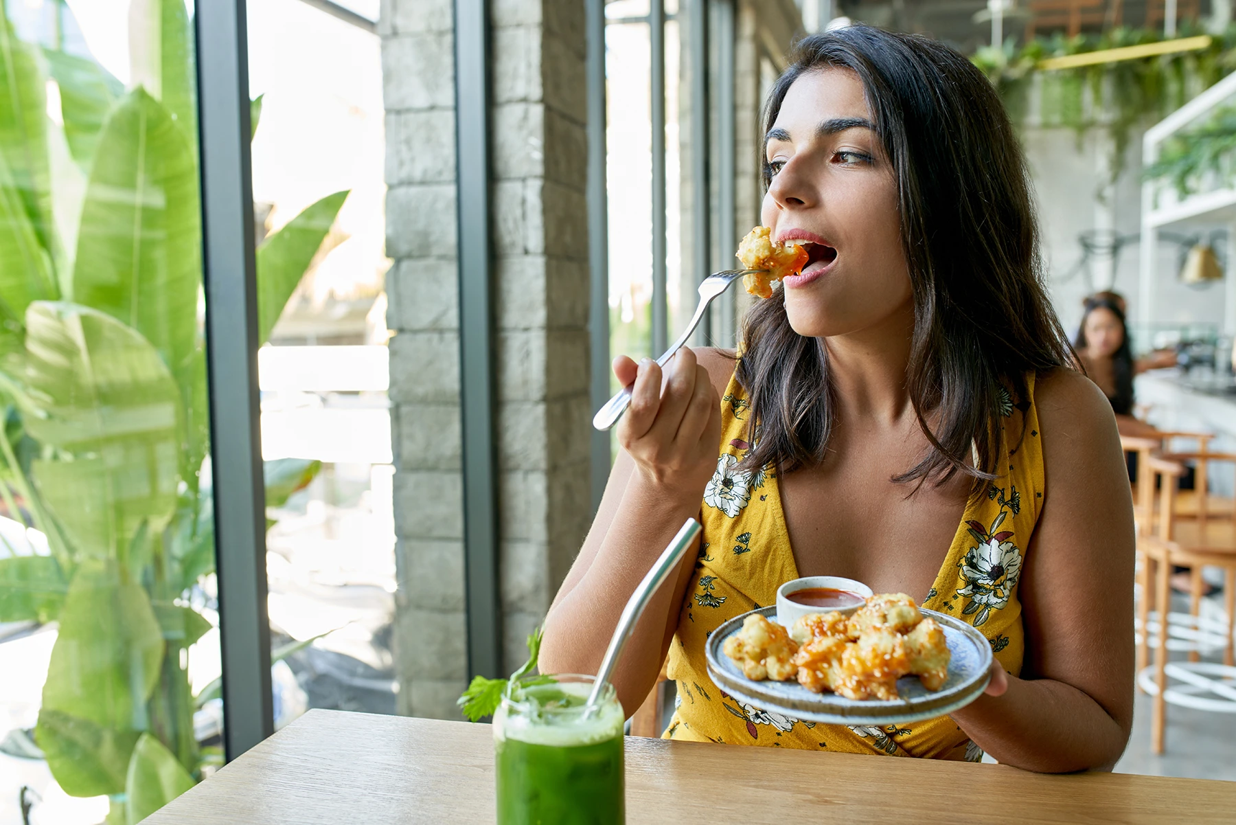 Woman eats cauliflower snack while drinking green smoothie.