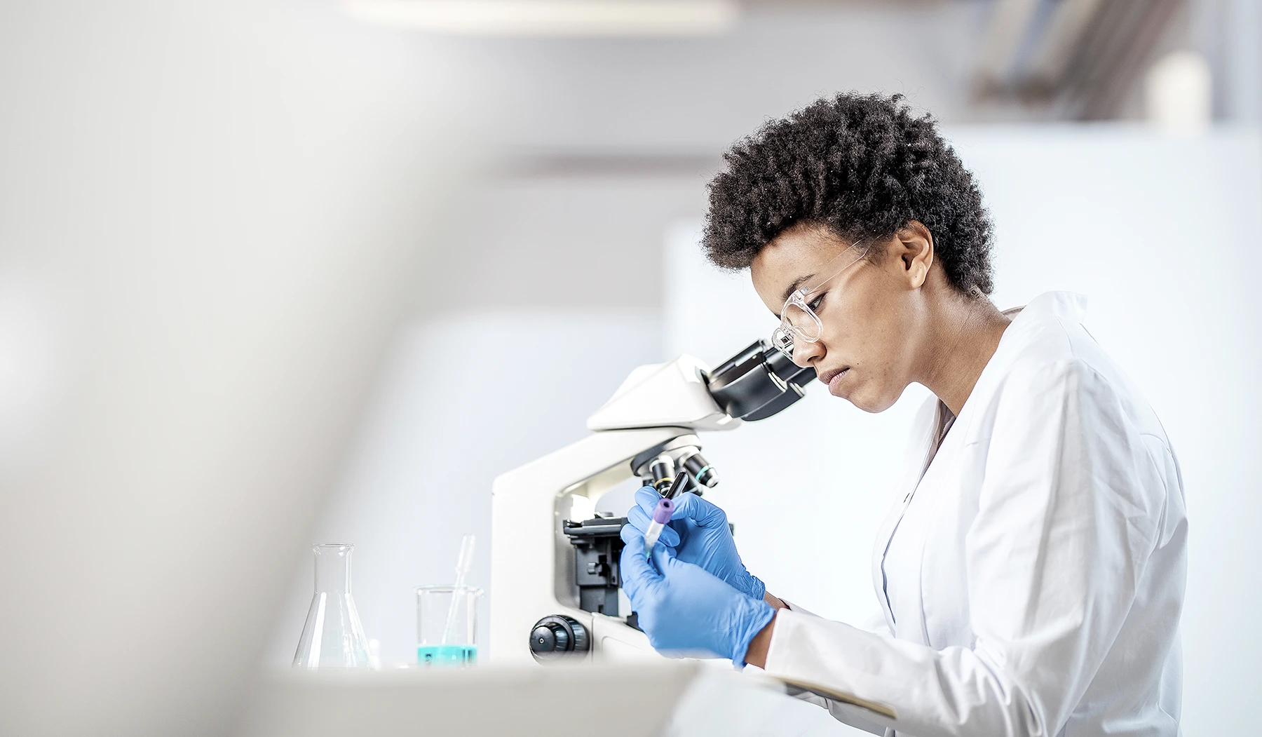 Stock image of a researcher in a lab looking at through a microscope.