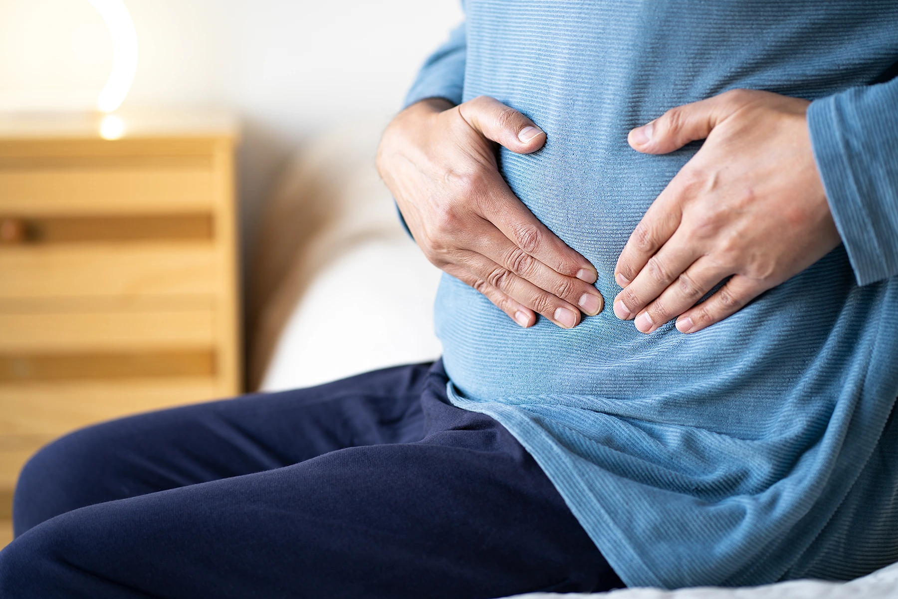 Close up of man in blue shirt holding his stomach in pain.