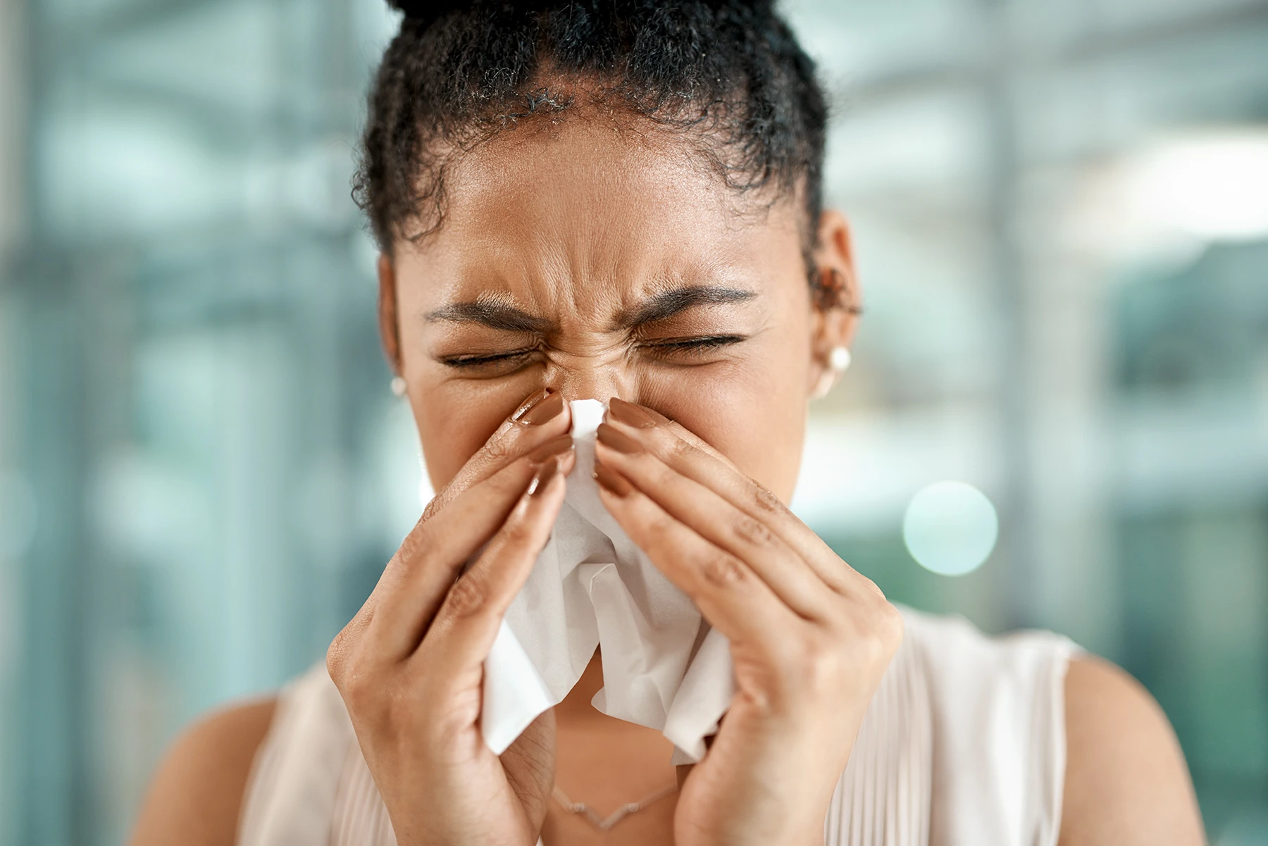 Pretty Hispanic woman is blowing her nose into a tissue due to allergies or sinus congestion.