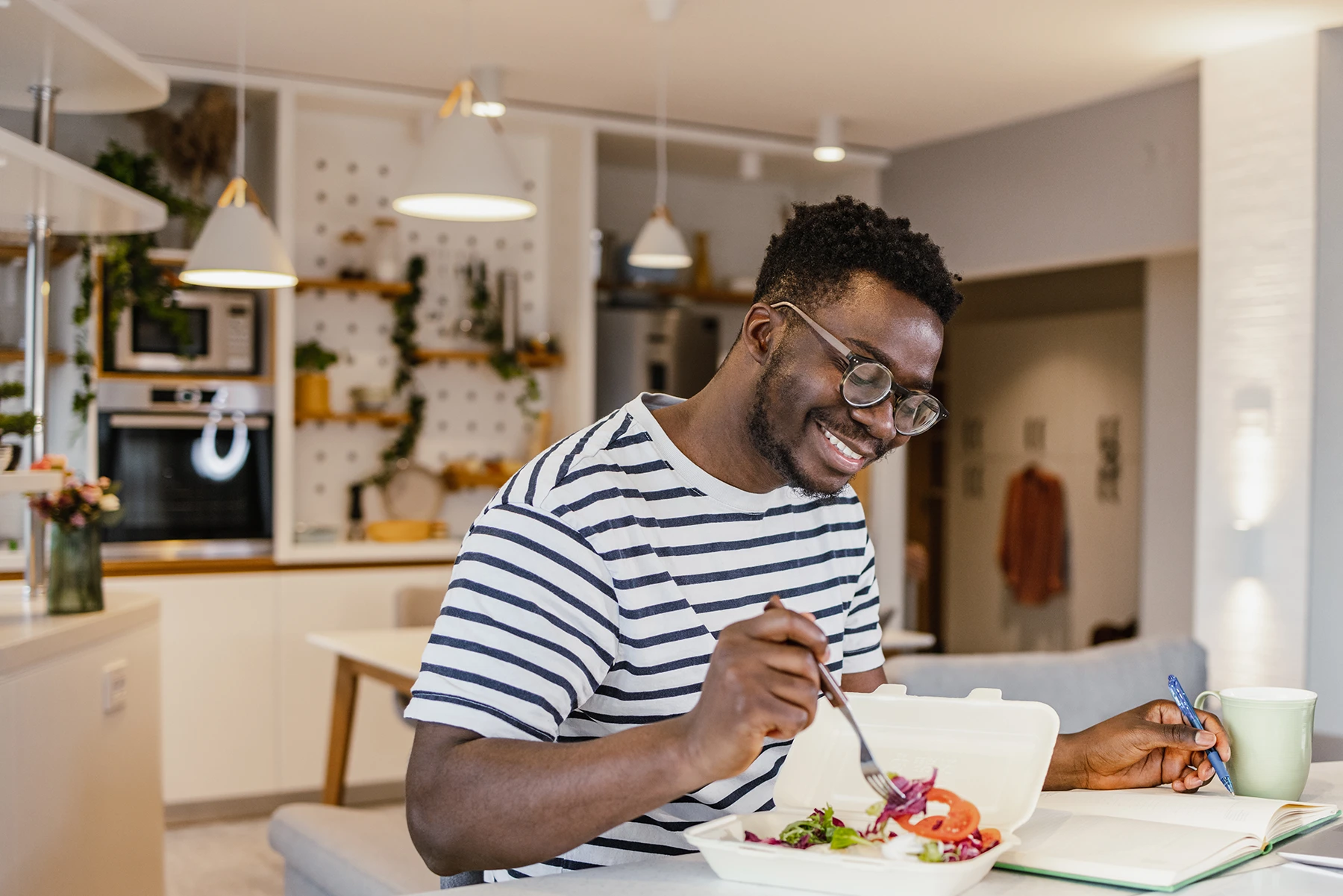 Happy young Black man eats at a table in his house.